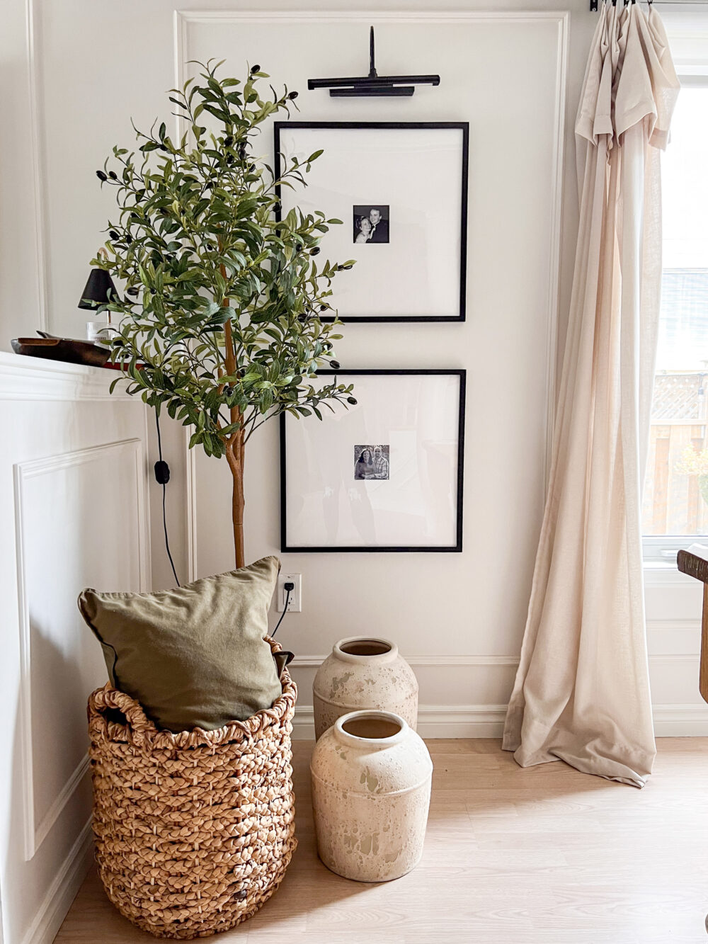 Faux olive tree beside a basket and two decorative jars.