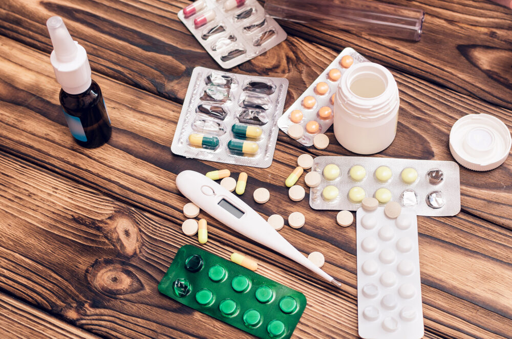 medicines, thermometer and nasal spray on a wood table