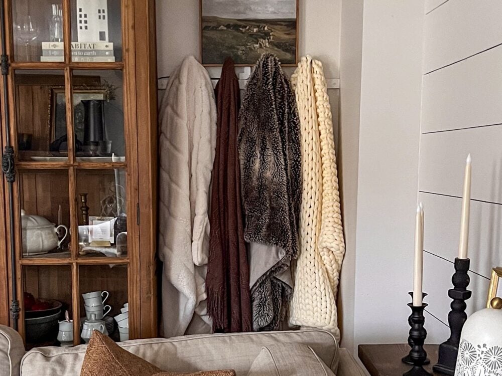 Living room blanket wall with chunky knit blankets and faux fur blankets. To illustrate Blanket Storage Tips. 