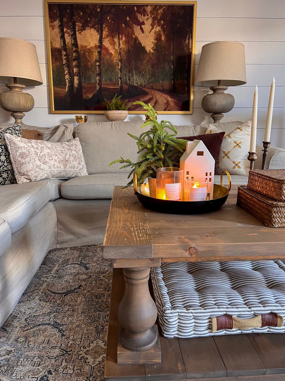 Lit candles on a metal tray on a coffee table in a cozy, farmhouse-style living room.